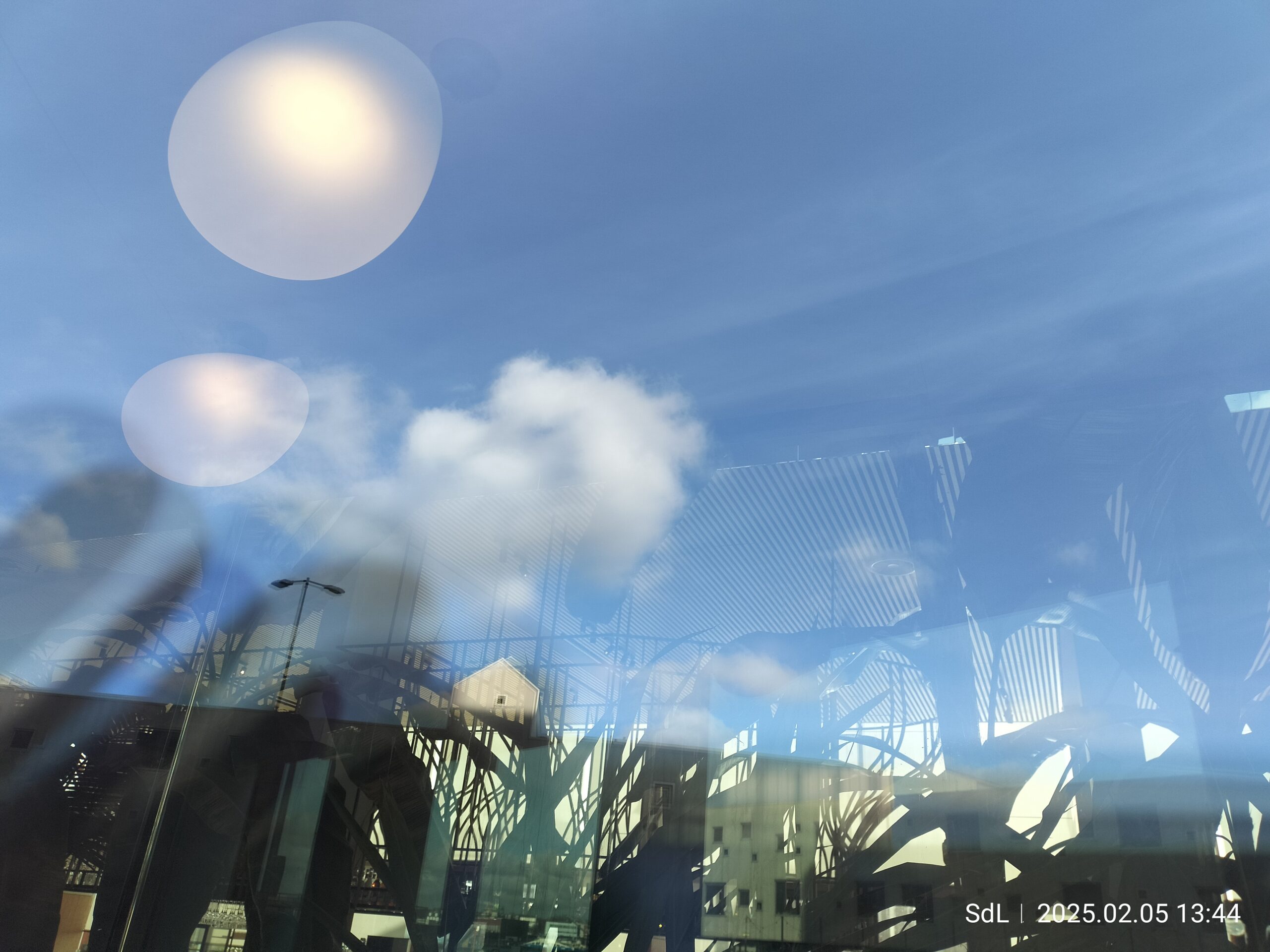 Wolken in een blauwe lucht weerspiegeld door grote ramen van een modern gebouw. Foto: Sacha de Leeuw